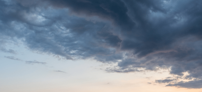 Small sailboat on a calm sea under dramatic storm clouds and a soft sunset.