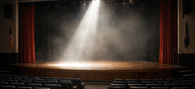 Empty theater stage lit by a spotlight with empty audience seats in front