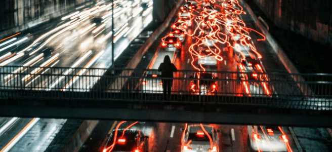 Cars with red and white light trails on a busy highway at night viewed from a pedestrian bridge