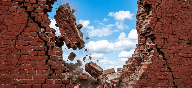 Red brick wall breaking apart with falling bricks and dust