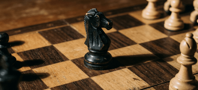 Black knight chess piece on wooden chessboard surrounded by pawns and other chess pieces