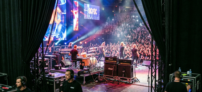 Backstage view of a live rock concert with band on stage and crew managing equipment