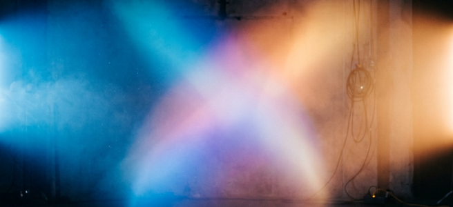 Intersecting blue, purple, and orange stage light beams in a dark industrial space
