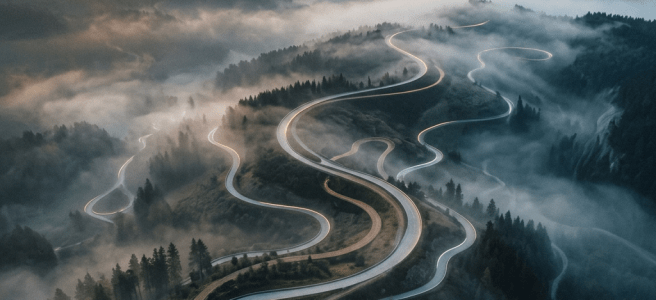 Curvy mountain road illuminated by vehicle lights winding through fog and dense forest