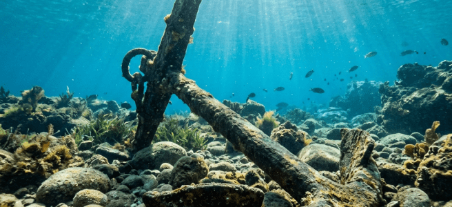 Rusty ship anchor resting on rocky seabed under clear water